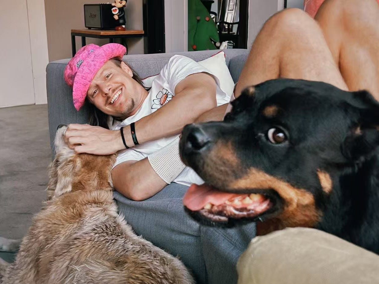 A man wearing a pink hat and laying on couch with two dogs.