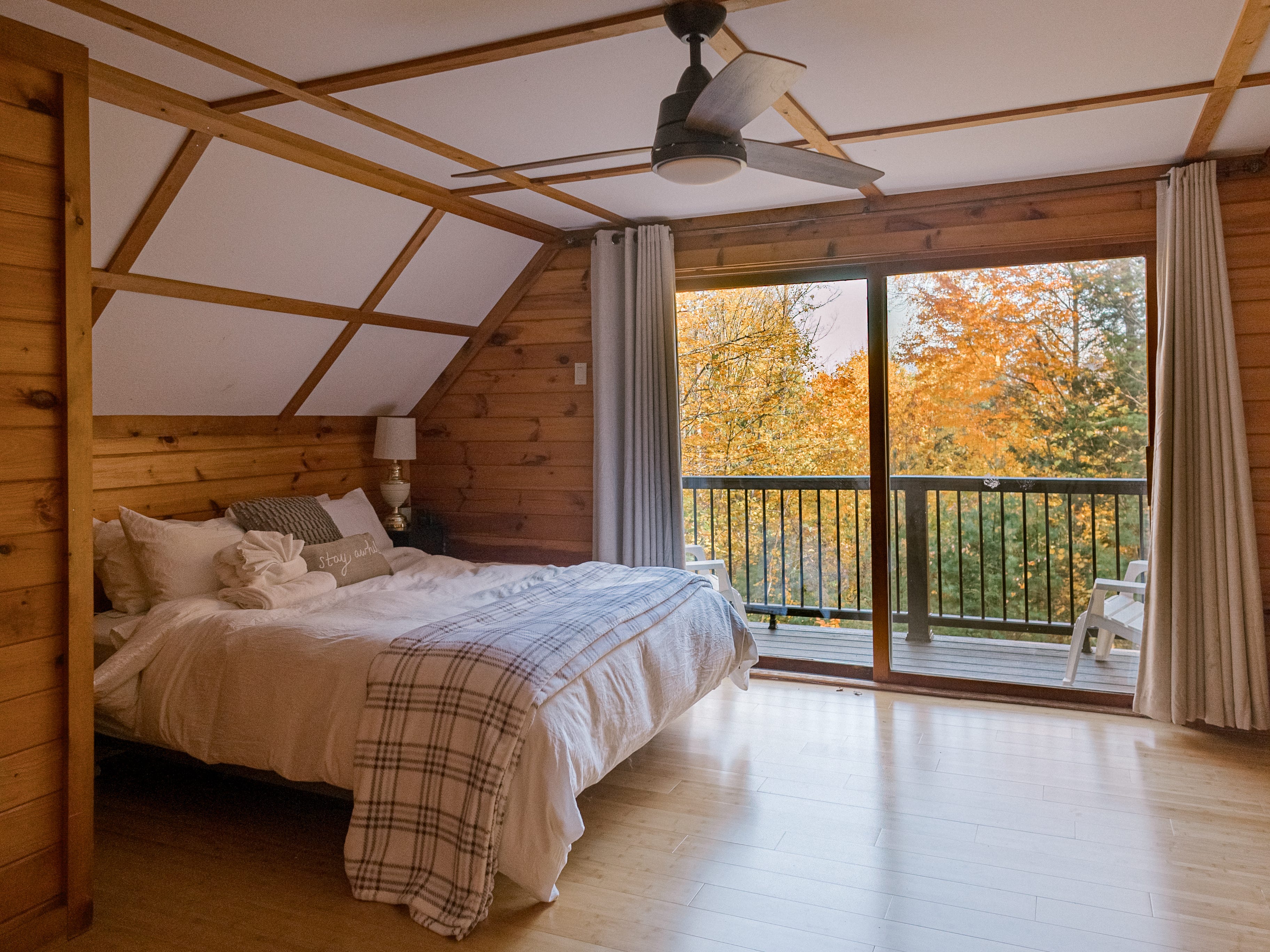 Bedroom with white ceiling with wooden beams above a bed, balcony nearby