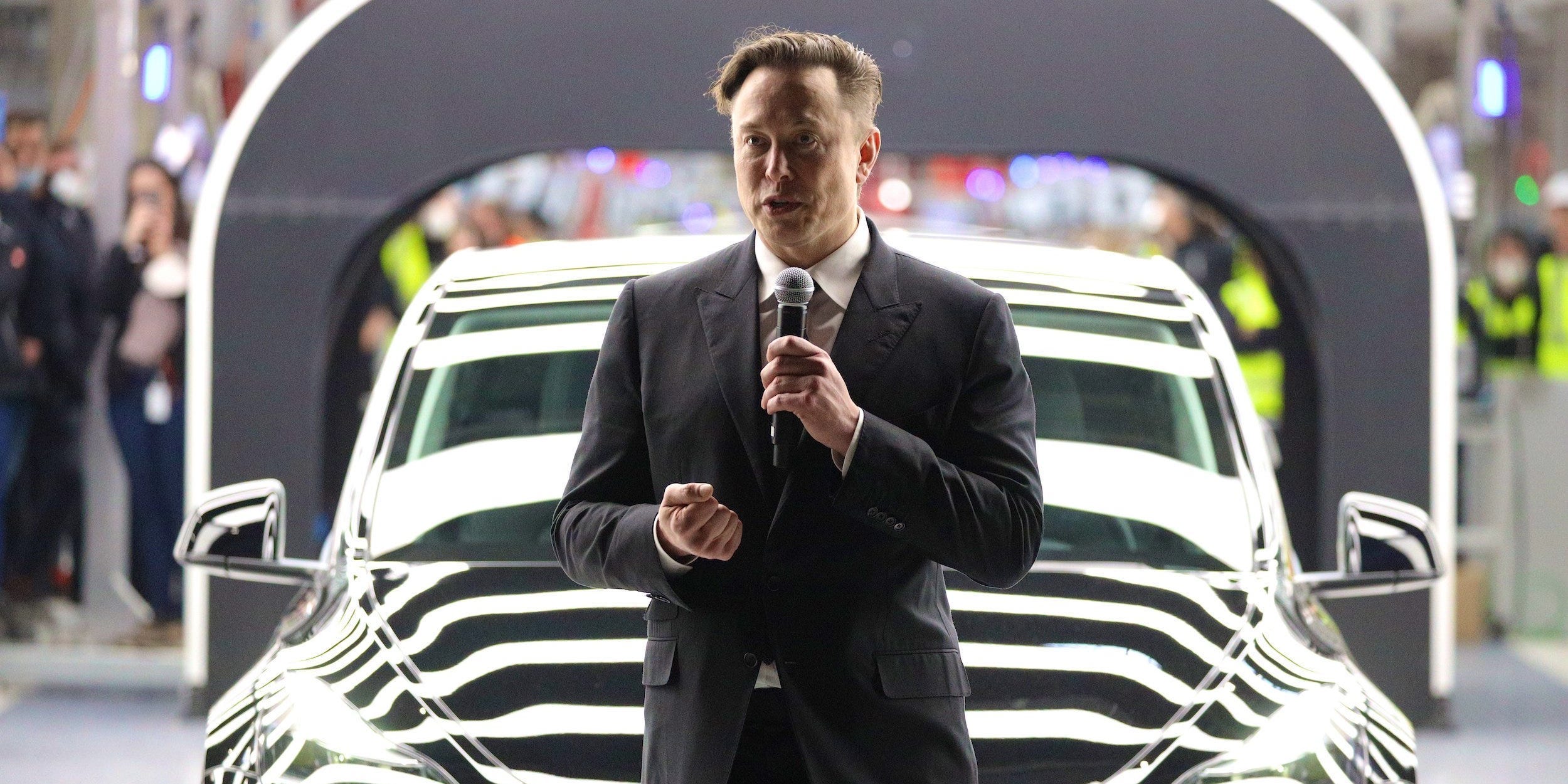 Elon Musk in front of a car, holding a microphone.