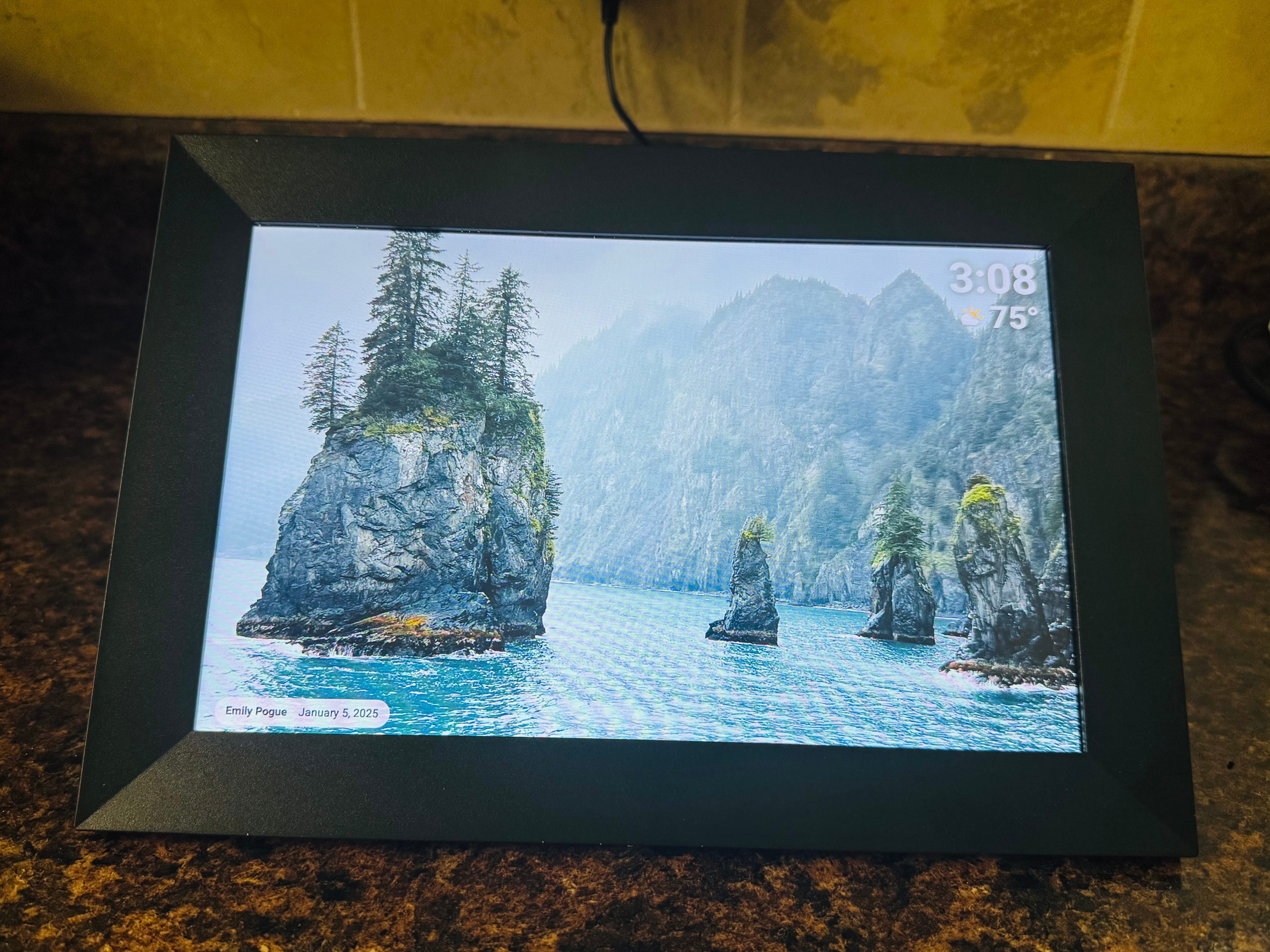 A digital photo frame on a counter displaying a wallpaper of floating rock formations.