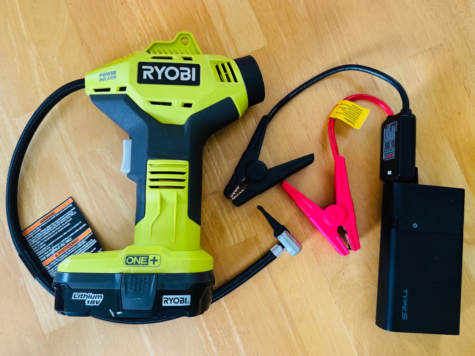 On the left, a portable tire inflator. On the right, a rechargeable jump starter with one black wire and one pink wire attached.
