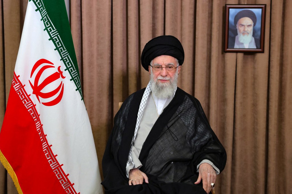 Ayatollah Ali Khamenei sitting in front of the Iranian flag.