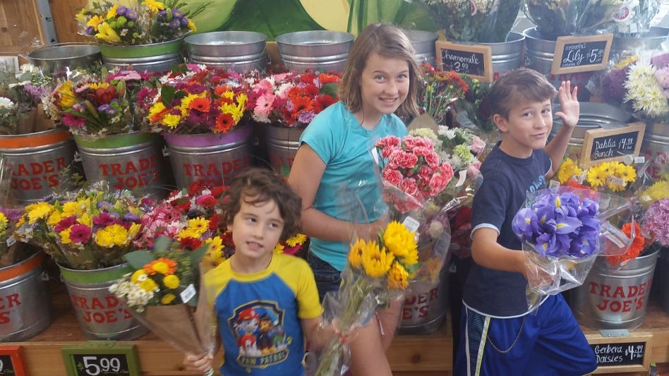 Three children pose in front of the floral display at a Trader Joe's store.