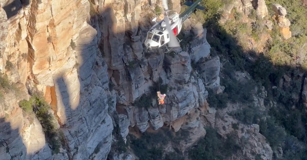 Helicopter rescuing a person from a rocky cliff.
