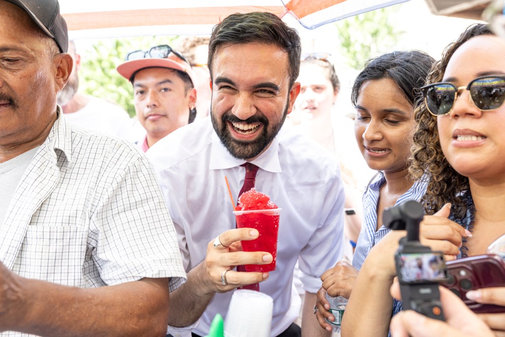 NYC mayoral candidate Zohran Mamdani smiling while holding a red snow cone.