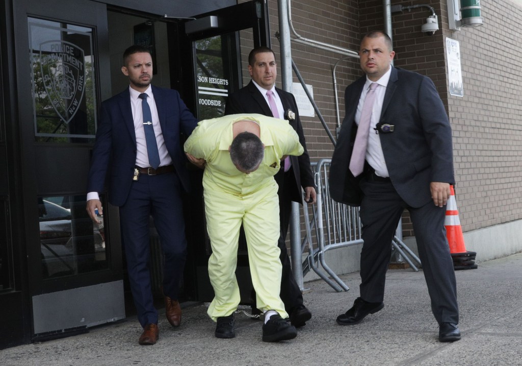 A man in a yellow jumpsuit escorted by two police officers.