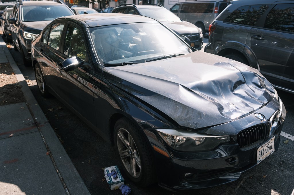 Damaged black BMW sedan parked on city street.