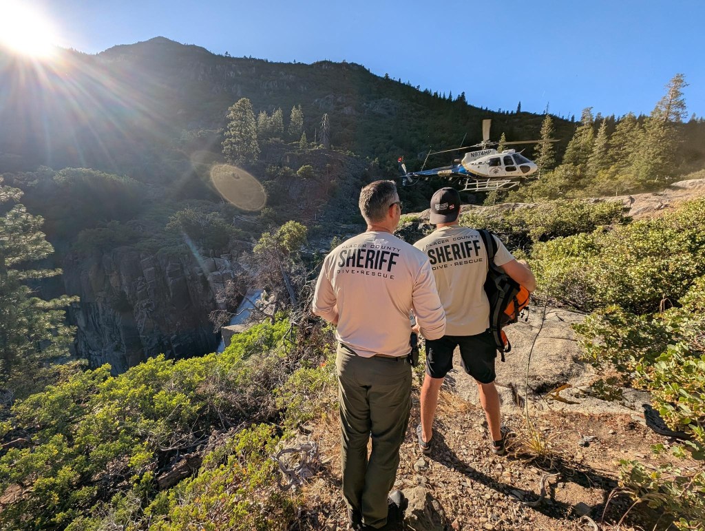 Two Placer County Sheriff Dive Rescue personnel watching a helicopter near a waterfall.