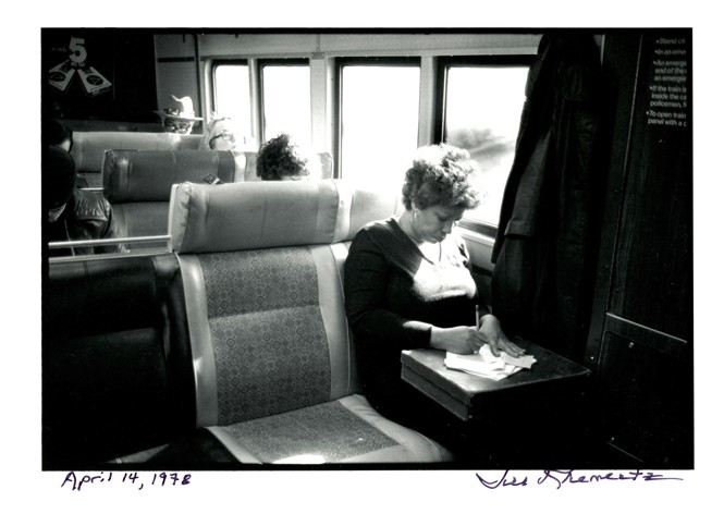 a black and white photo of the novelist Toni Morrison sitting on a train and writing on a stack of papers