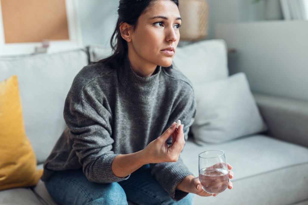 Woman sitting on a couch, holding a pill and a glass of water.