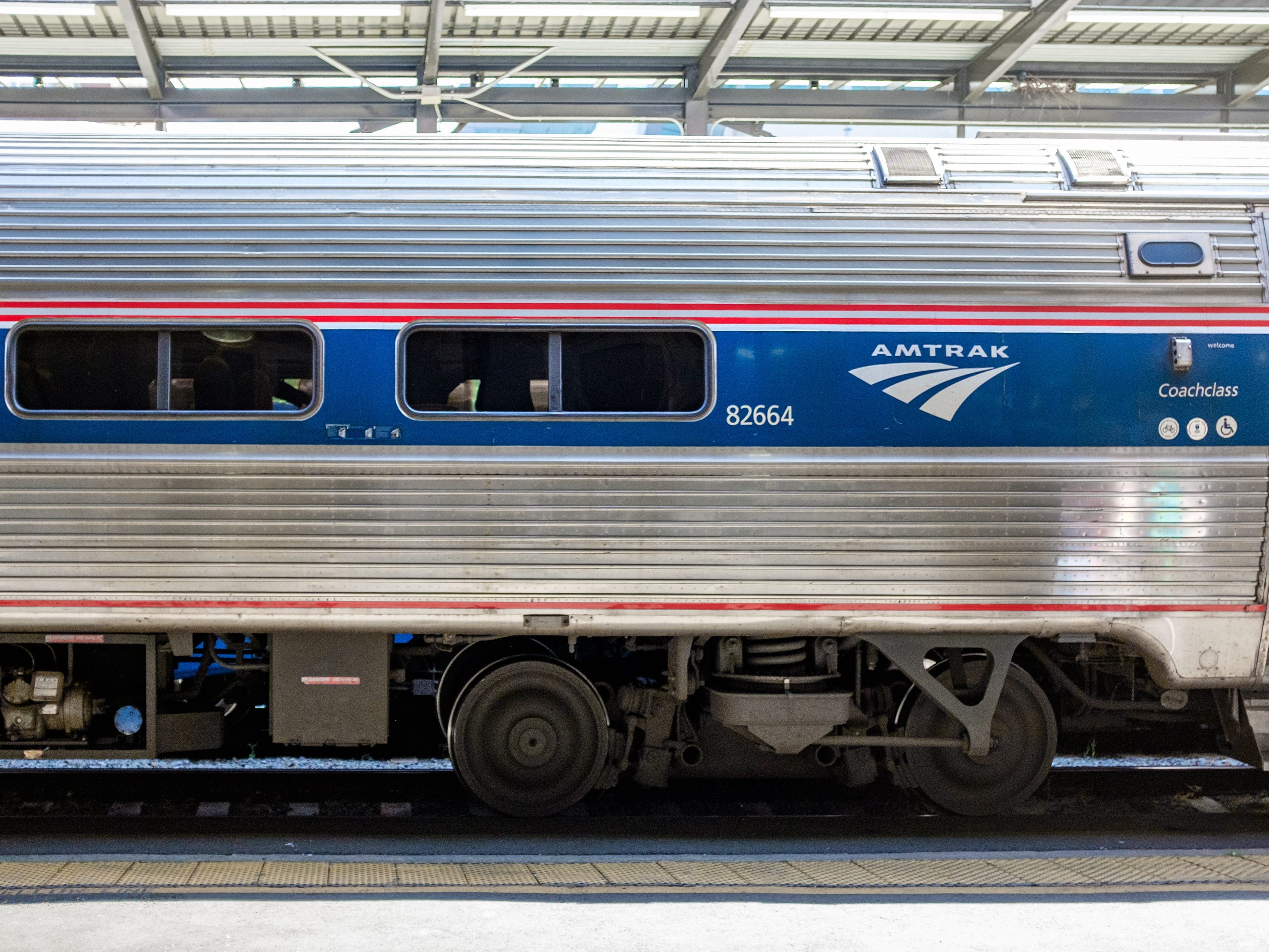The exterior of a coach Amtrak train car with an attendant stepping out a door on the right
