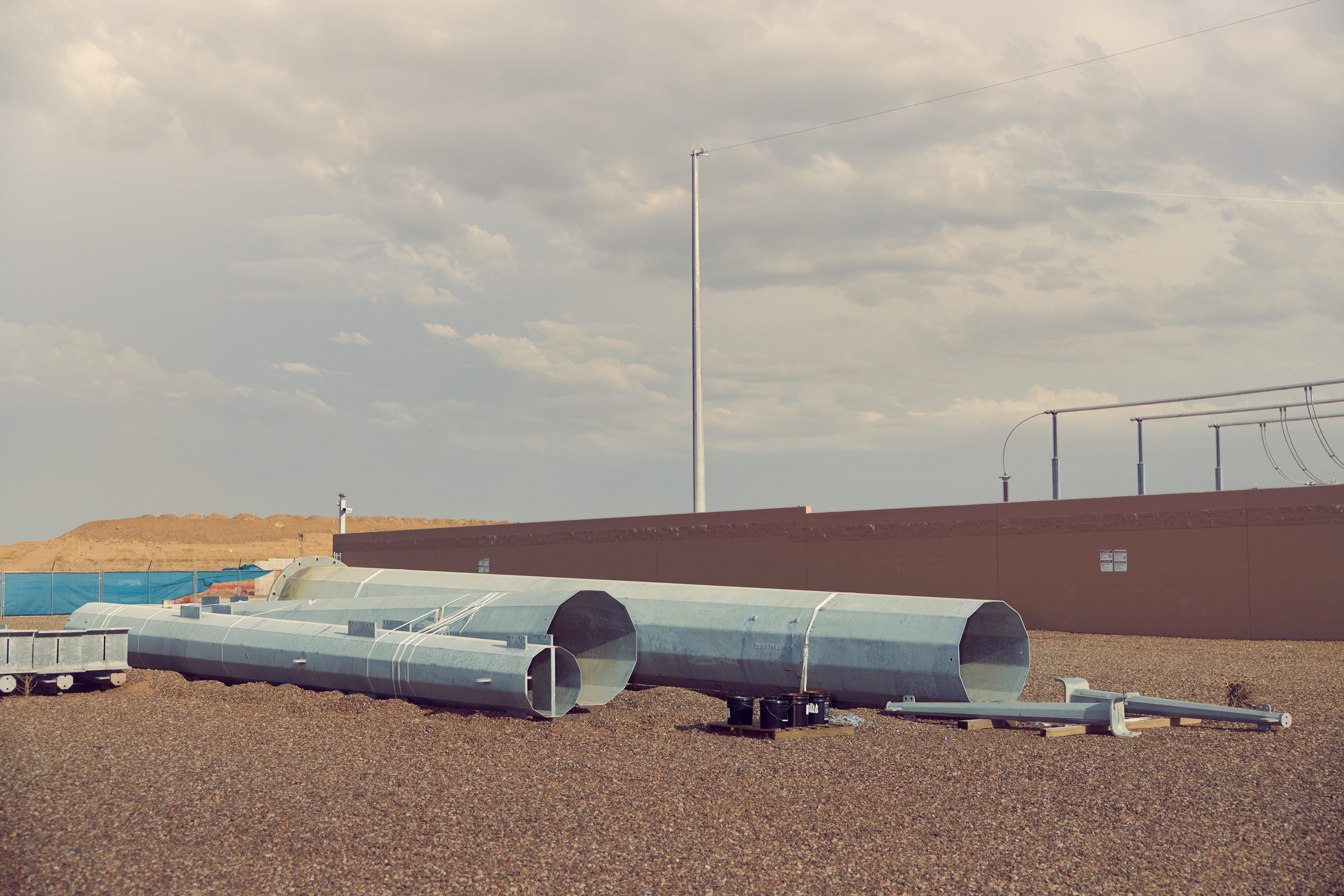 Large metal pipes laid out on gravel near an industrial site.