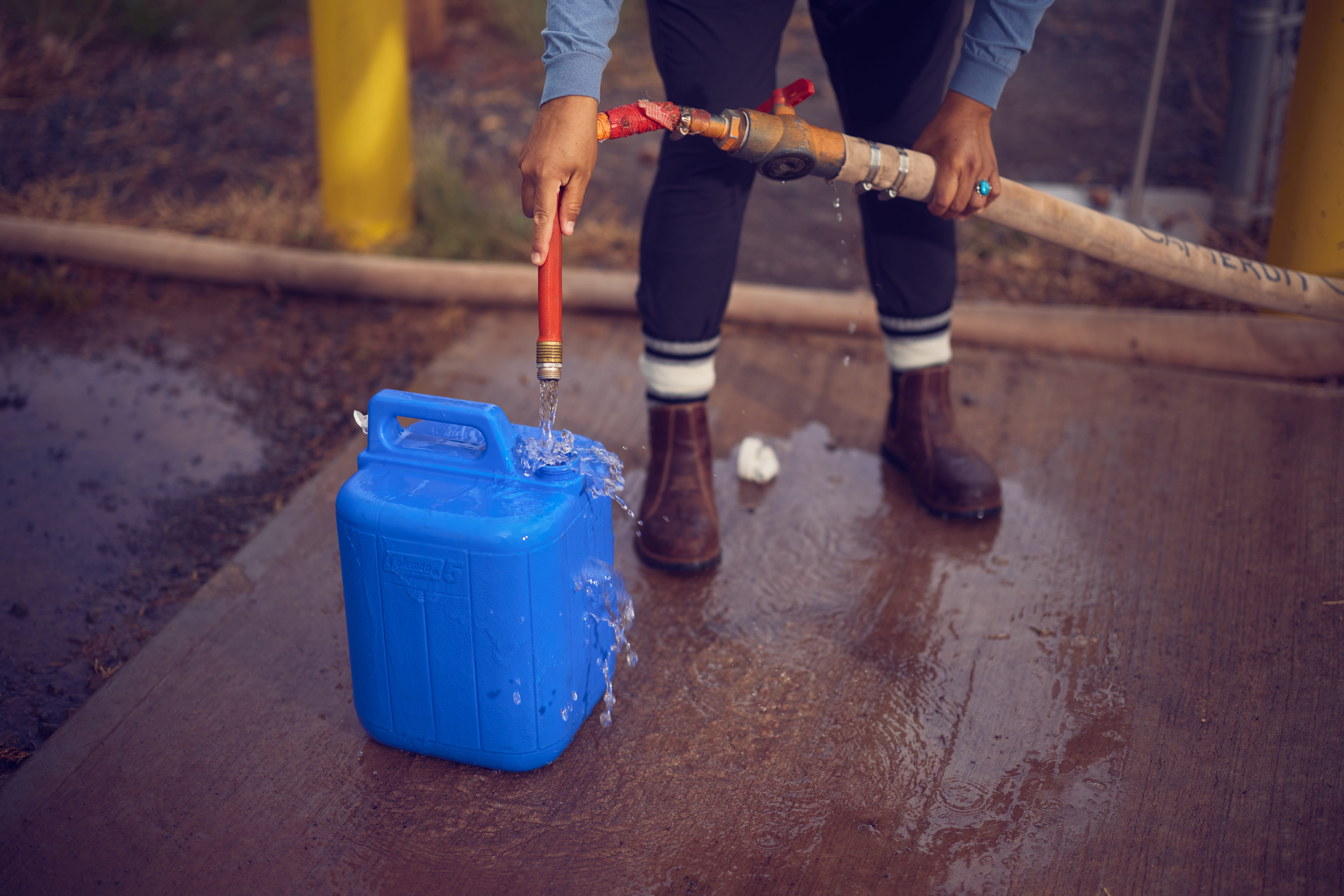 A person filling a blue container from a hose.