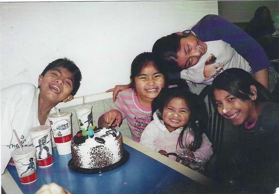 Viviana Vazquez smiles with her cousins and sister as they sit at a table in McDonalds with a cake and sodas on the table in front of them