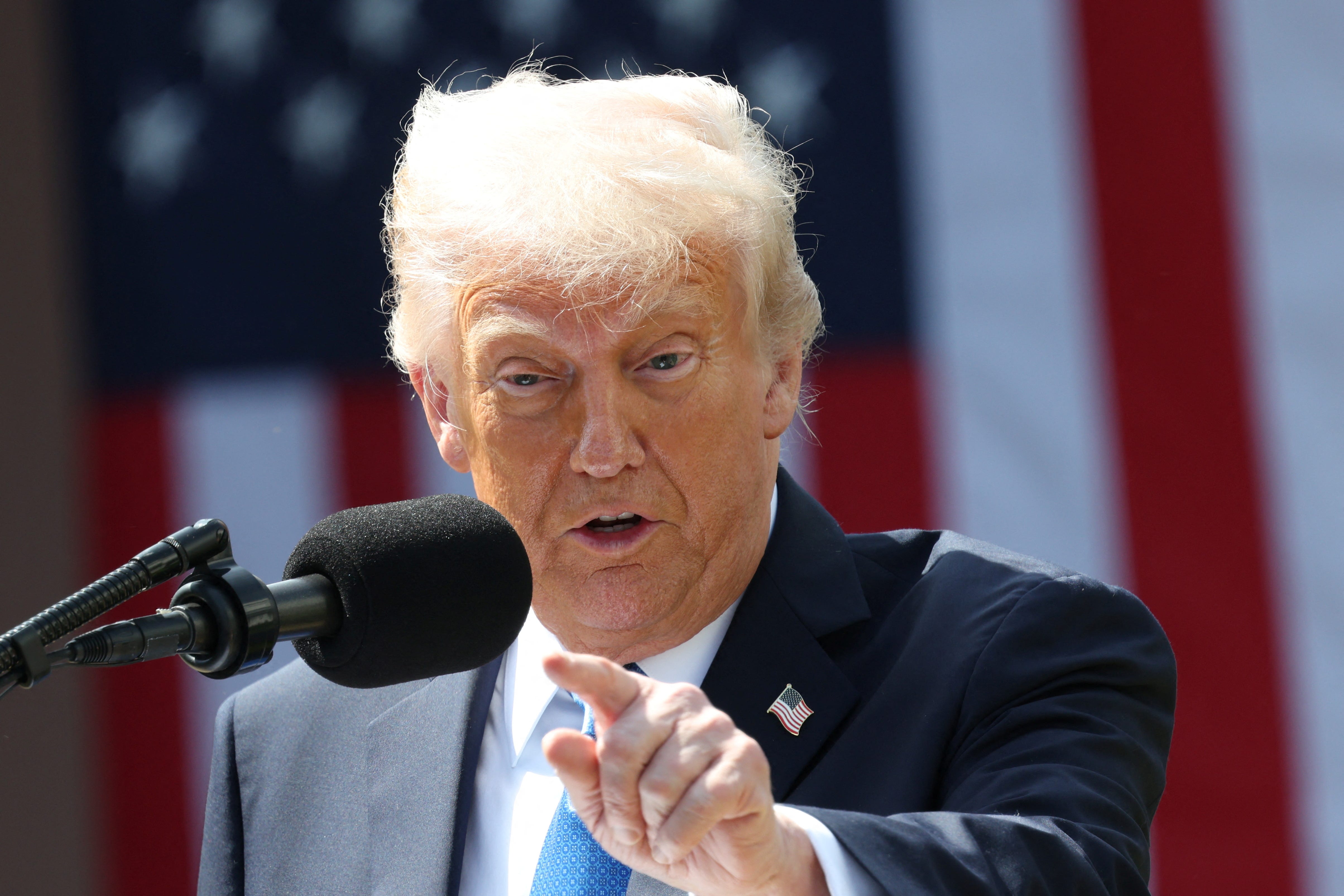 President Donald Trump speaking into a microphone and pointing. The US flag is behind him.