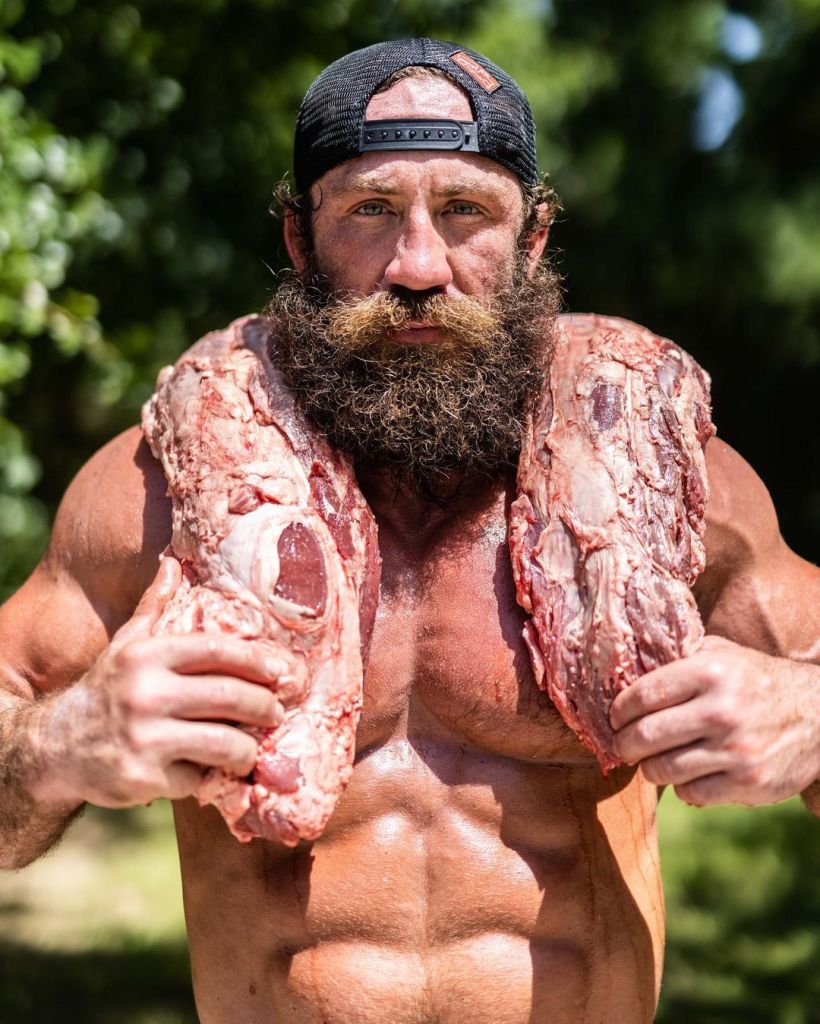 Muscular man holding large cuts of raw meat.