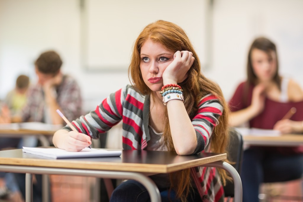 Bored female student taking notes in a classroom.
