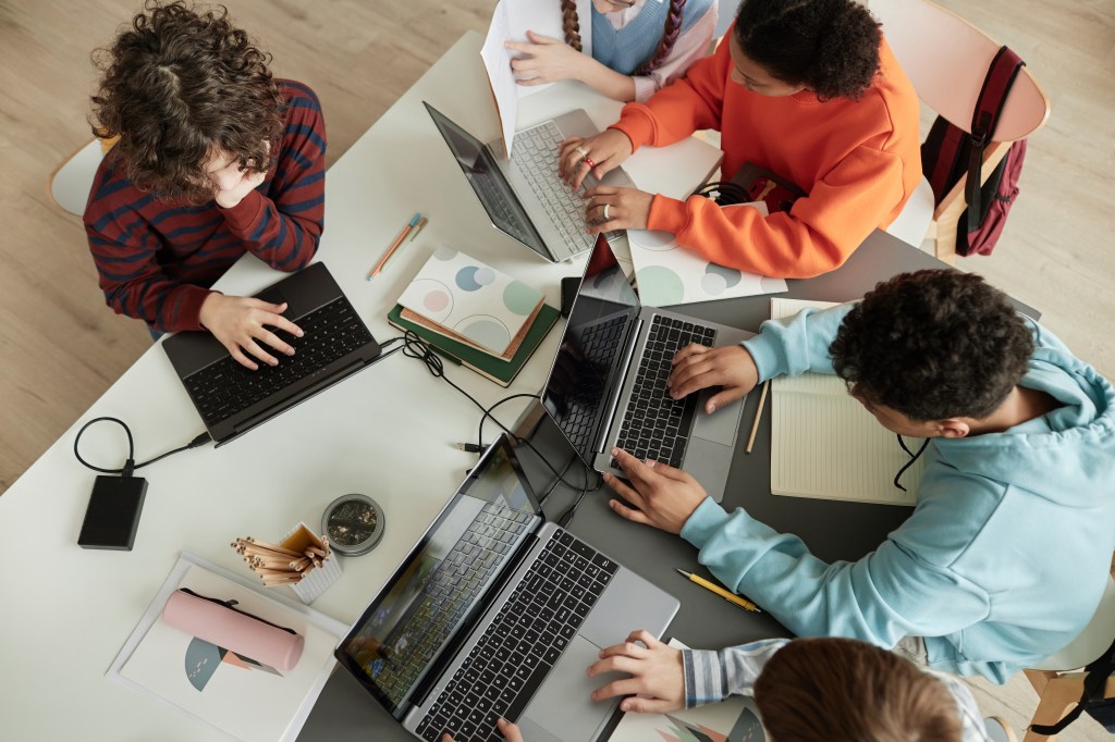 Overhead view of teenagers using laptops in a classroom.