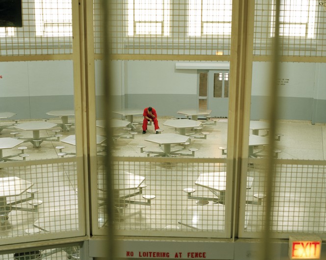 A color photograph of a man sitting along in a prison lunch room 