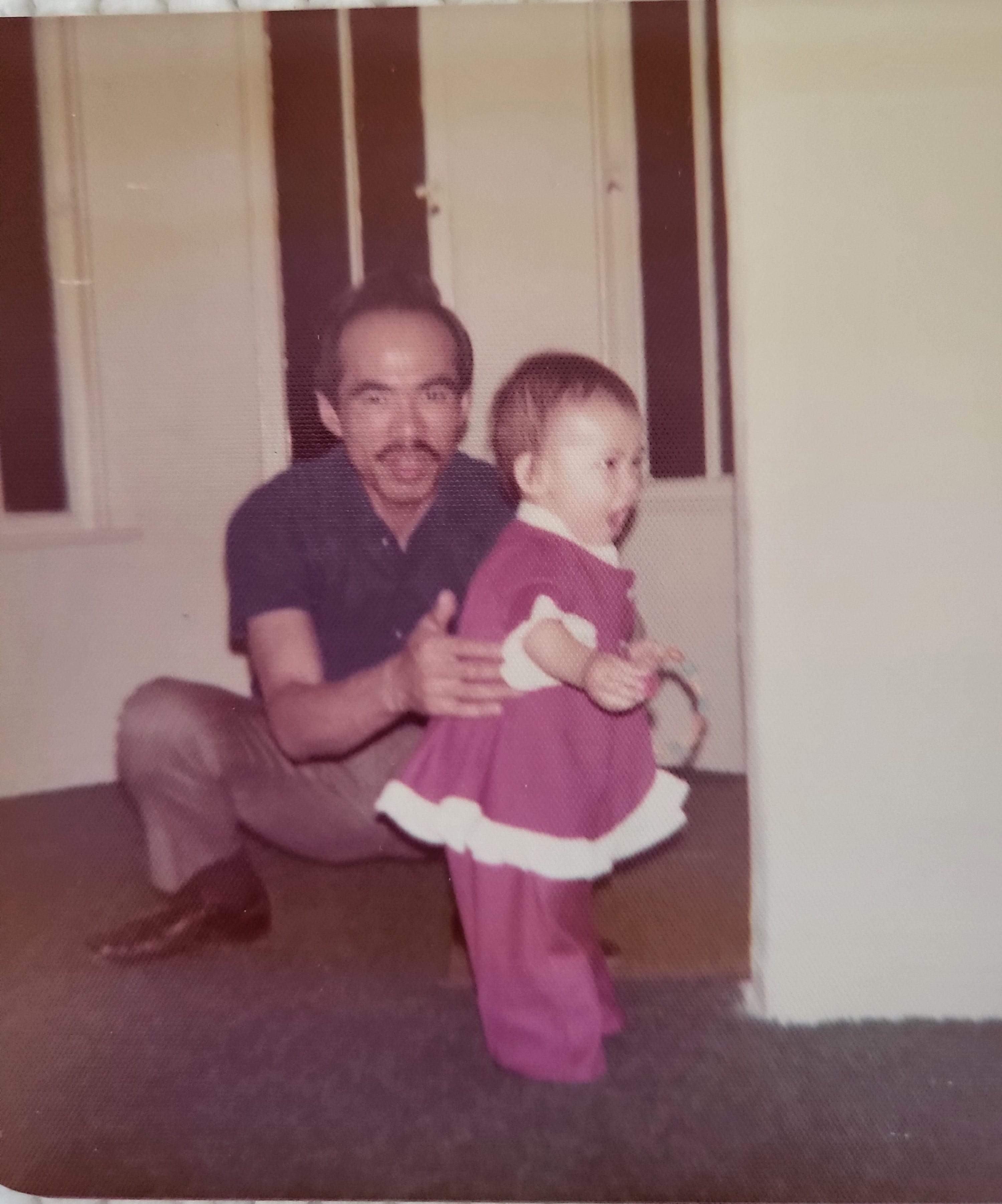 An old photo of a man teaching a little girl dressed in red how to walk.