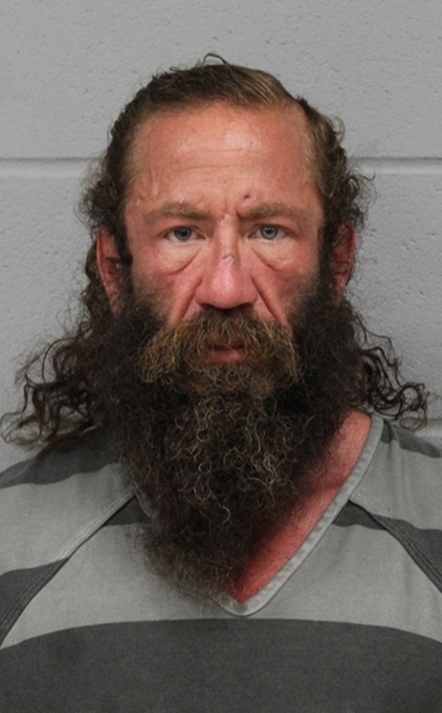 Mugshot of a man with long brown hair and a full beard, wearing a gray and black striped shirt.