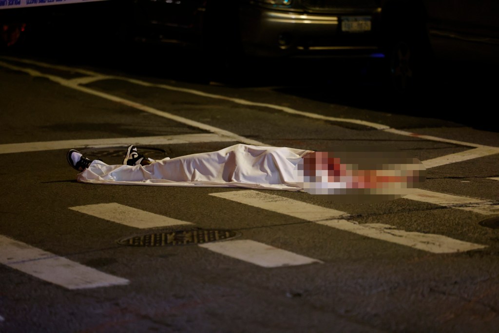 Body of a deceased woman covered in a white sheet on a city street.