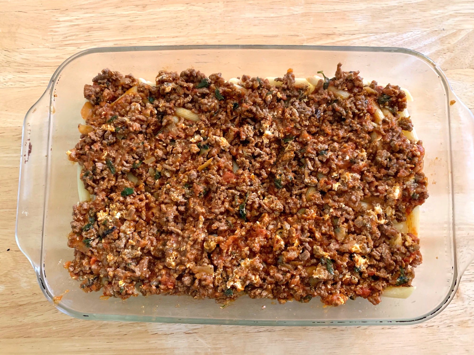 Ground beef mixture in top of pasta in glass baking dish
