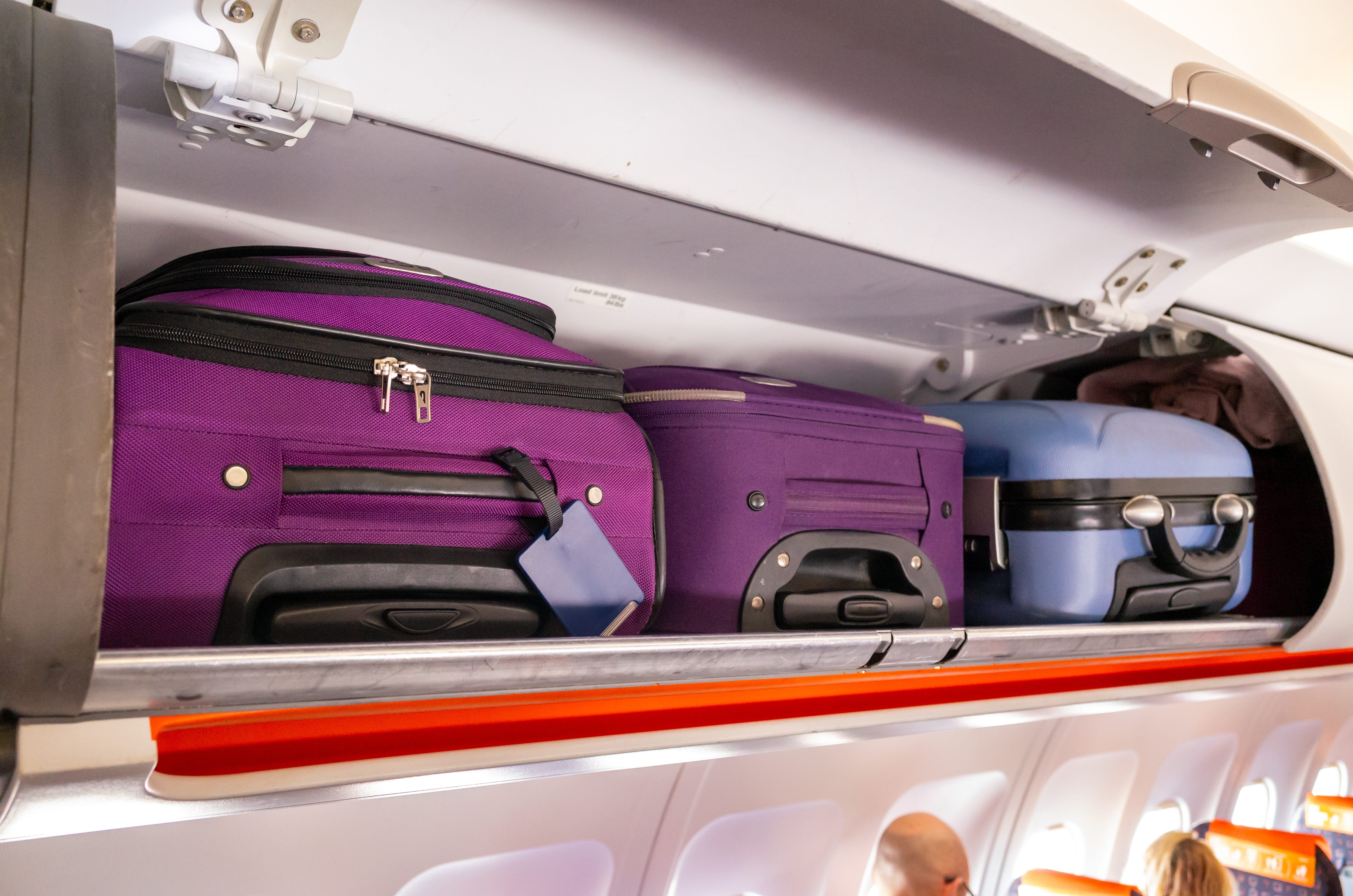 Suitcases in overhead luggage compartment on an airplane.