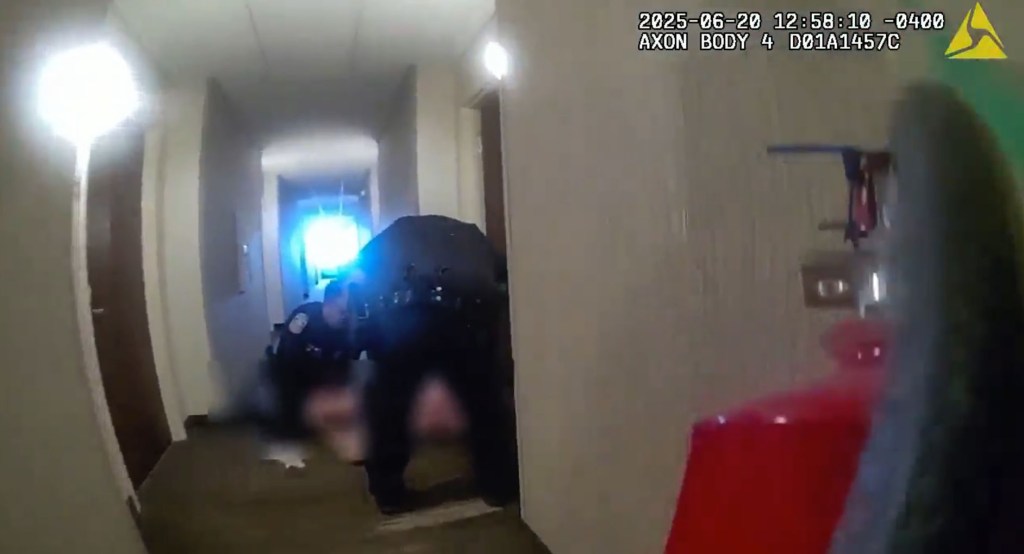Police officers detain Pitchford in the hotel hallway.