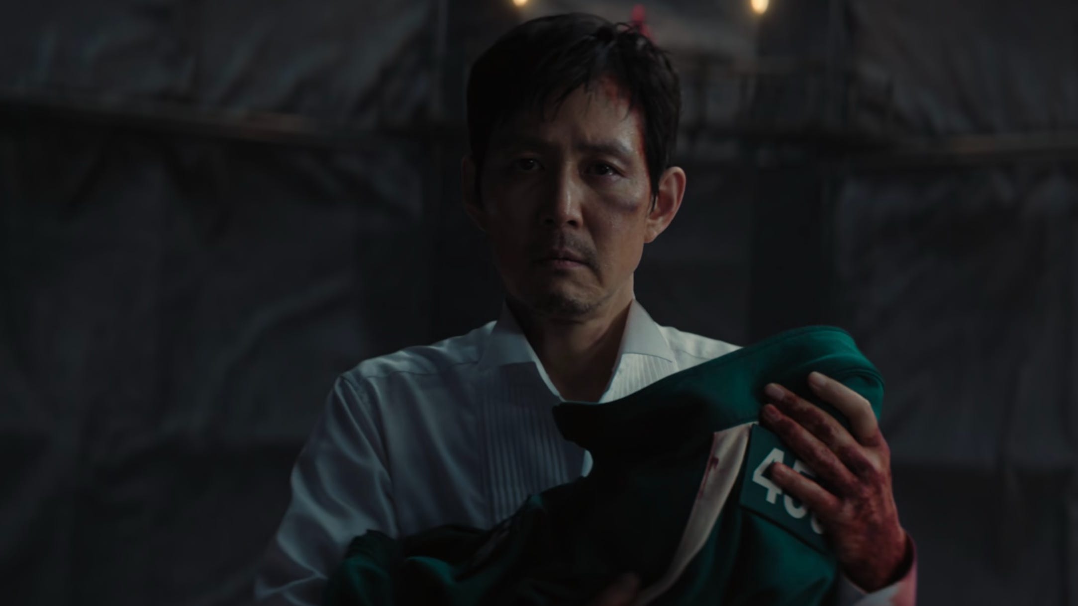 A screengrab of "Squid Game" showing Lee Jung-jae in a white shirt holding a green tracksuit.