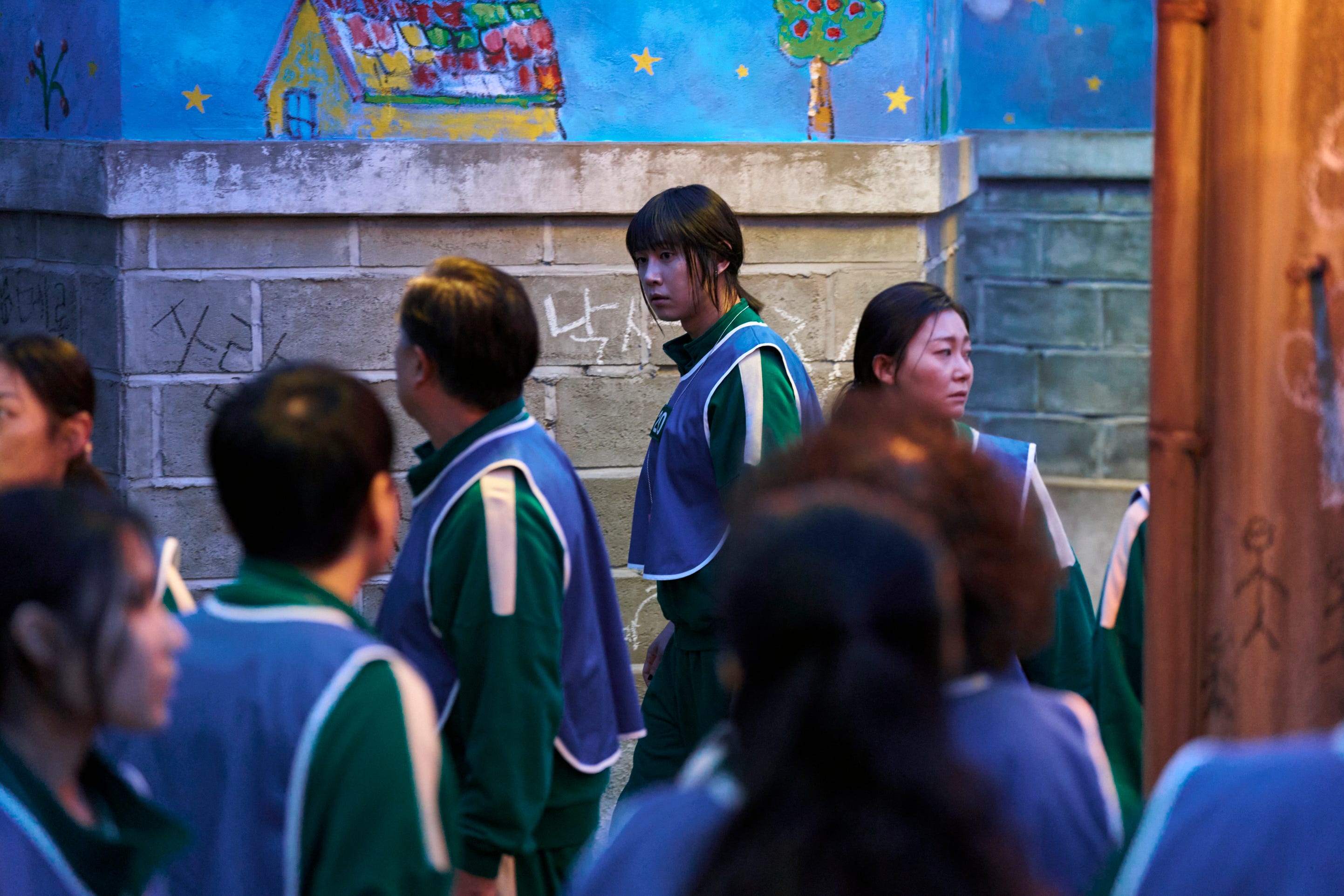 A still of "Squid Game" showing a group of people in matching green tracksuits and blue vests.