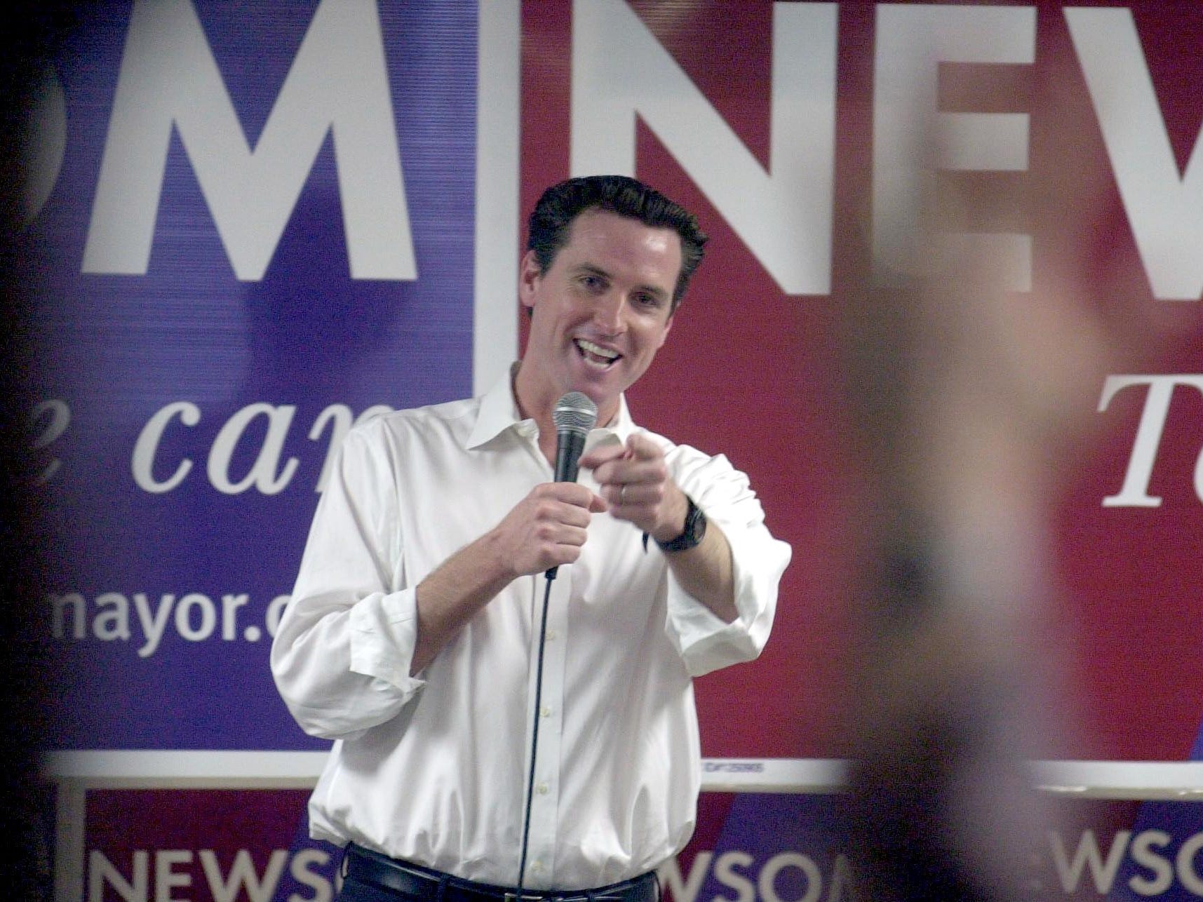 Mayoral candidate Gavin Newsom, posing in front of his campaign signs and speaks into a microphone while addressing volunteers at a campaign rally.