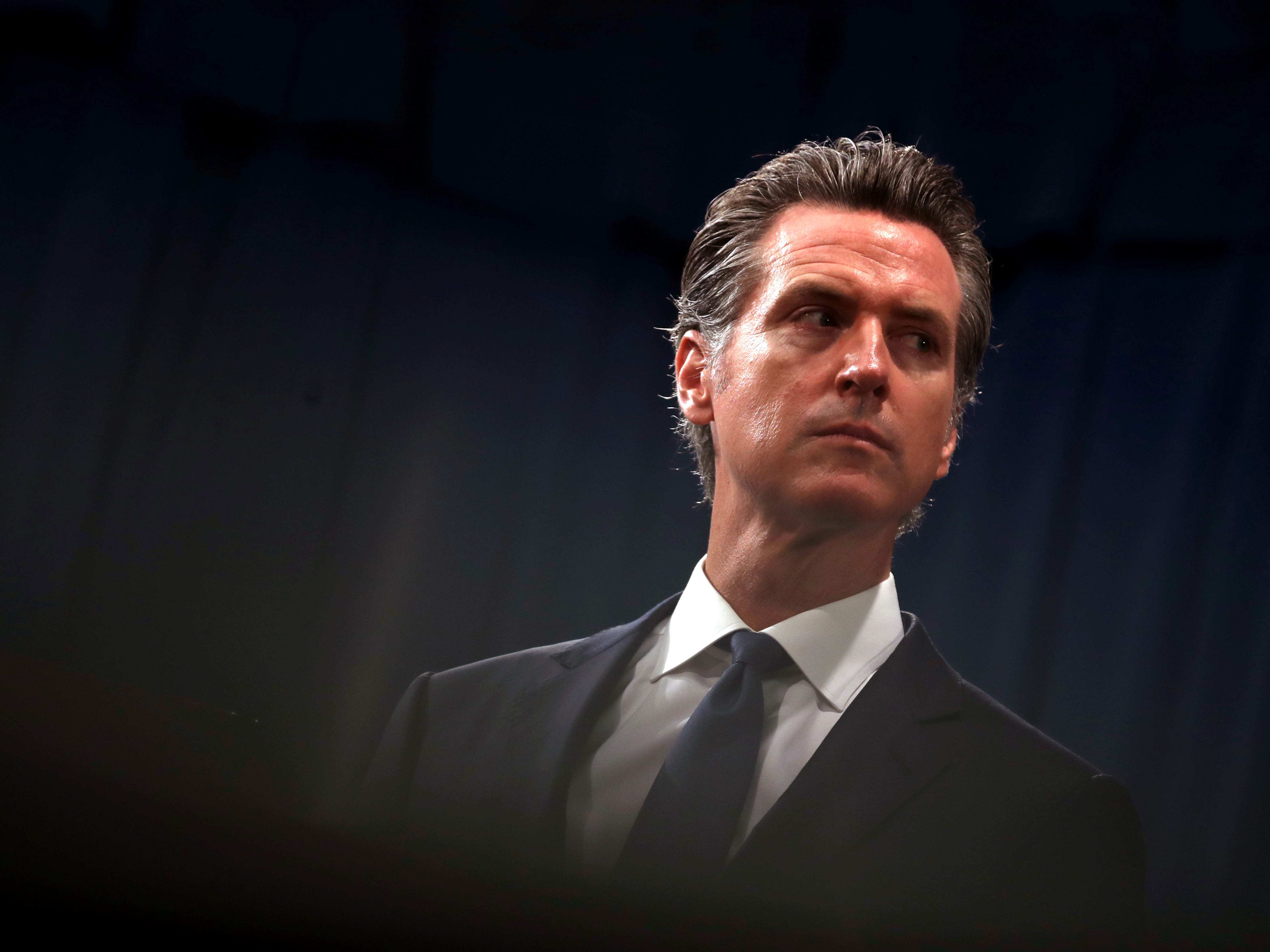 California Gov. Gavin Newsom looks on during a news conference, his face very serious.