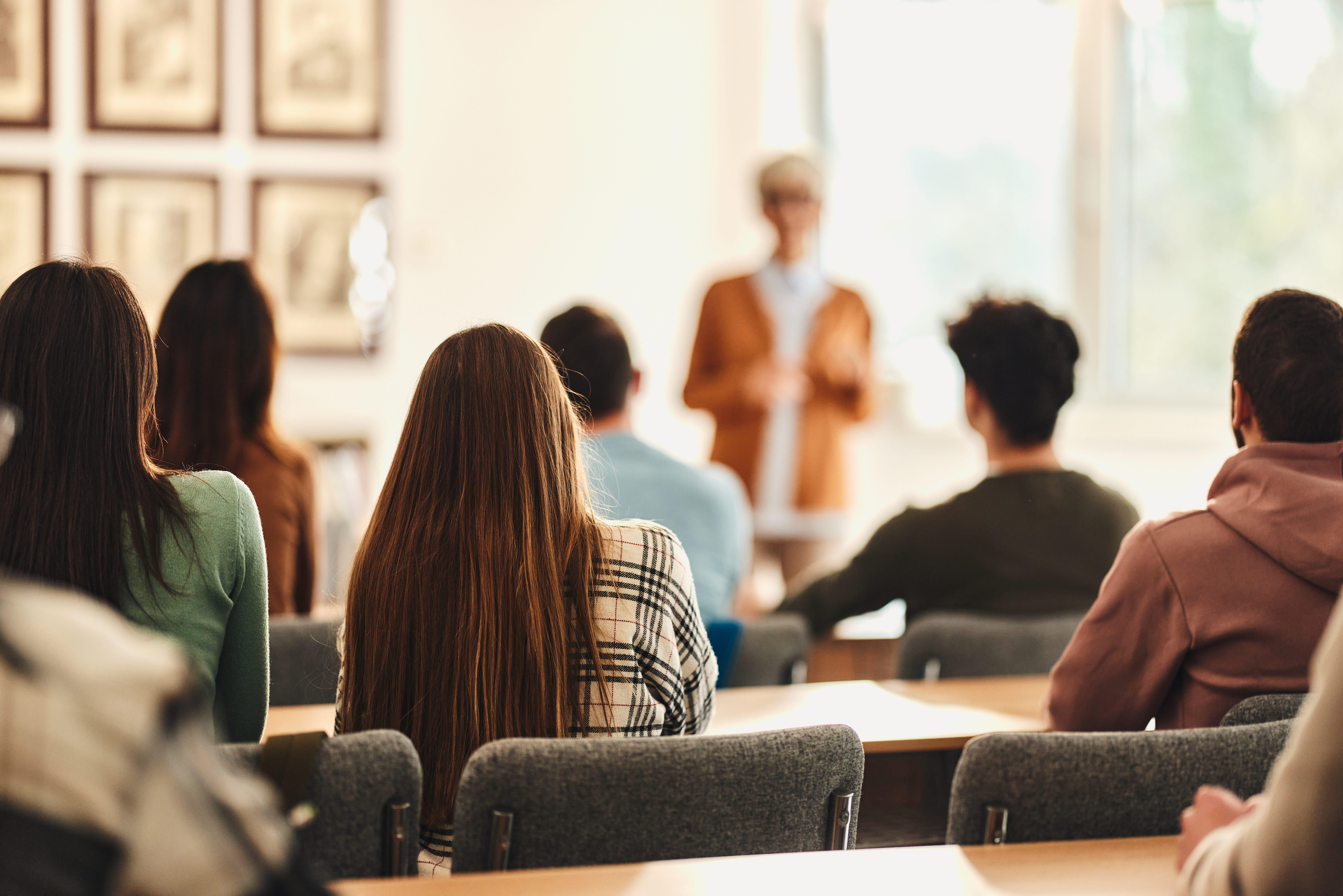 Rear view of large group of college students attending a class in lecture hall. Focus is on women in the middle.