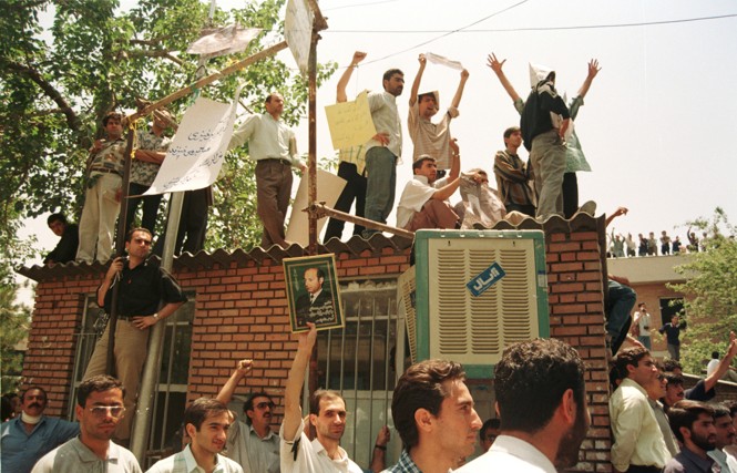 People march and hold signs up in a protest in Iran