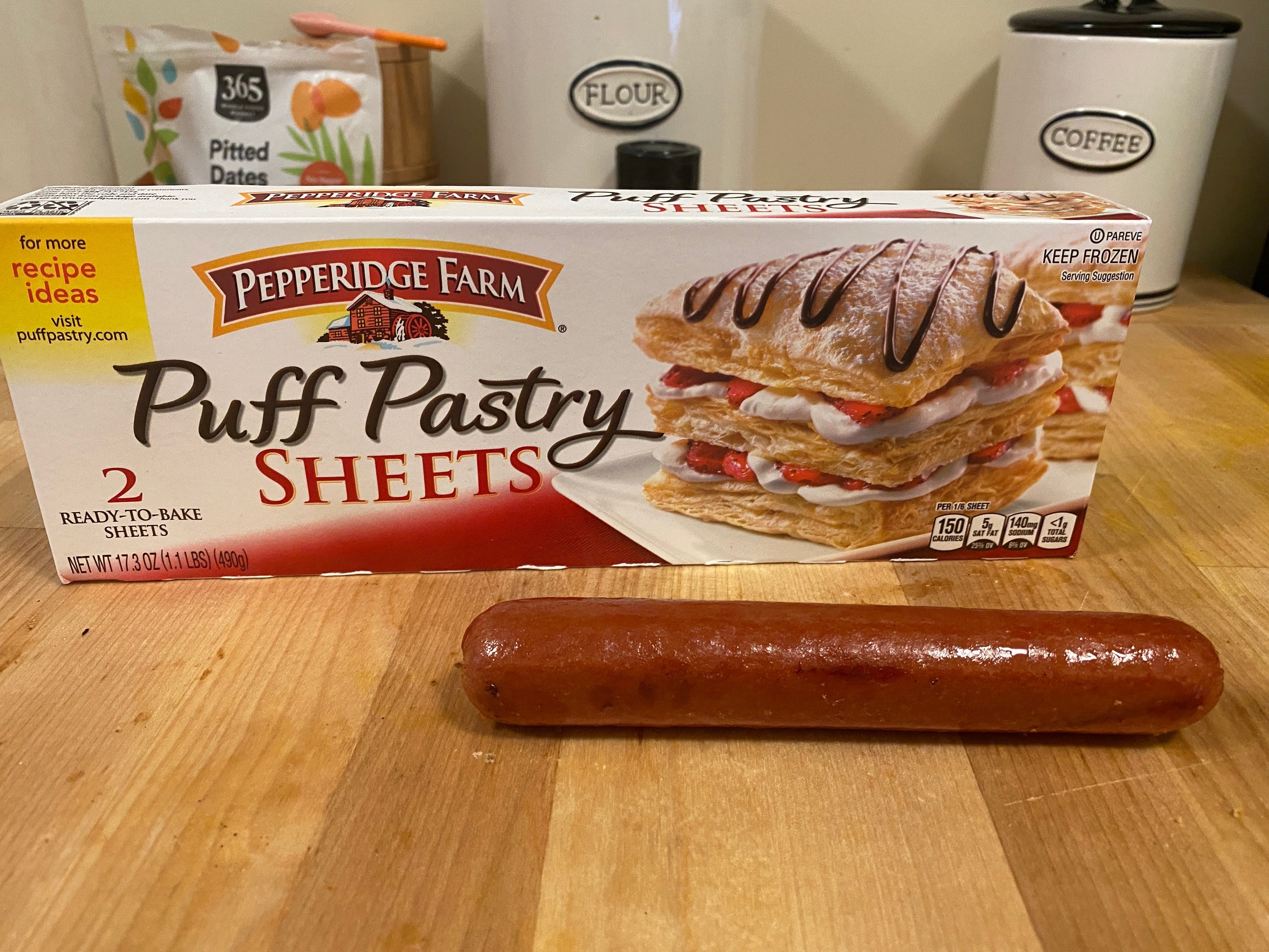 A photo of puff pastry sheets and a hot dog on wood