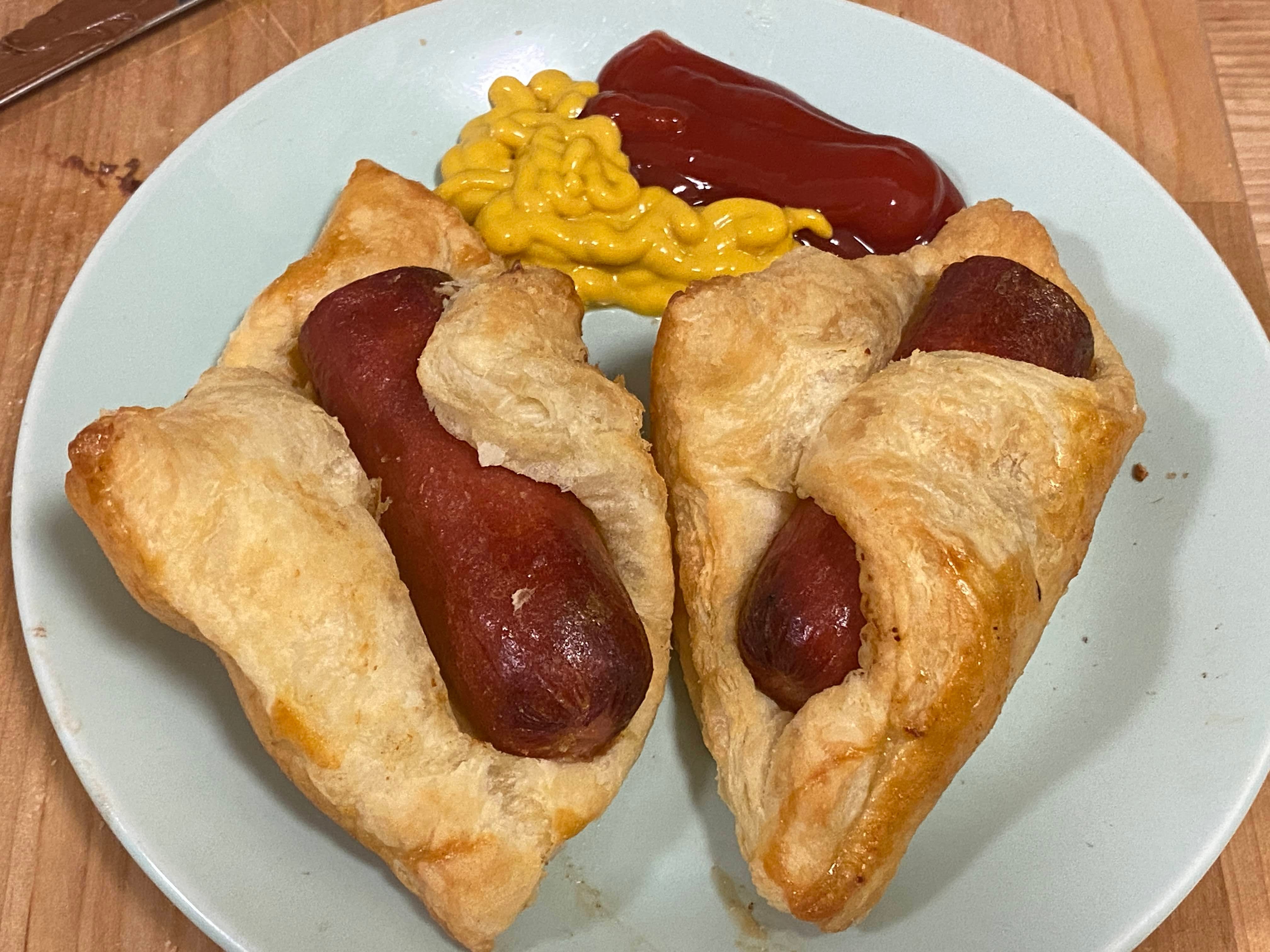 A photo of pigs in a blanket on a plate with ketchup and mustard