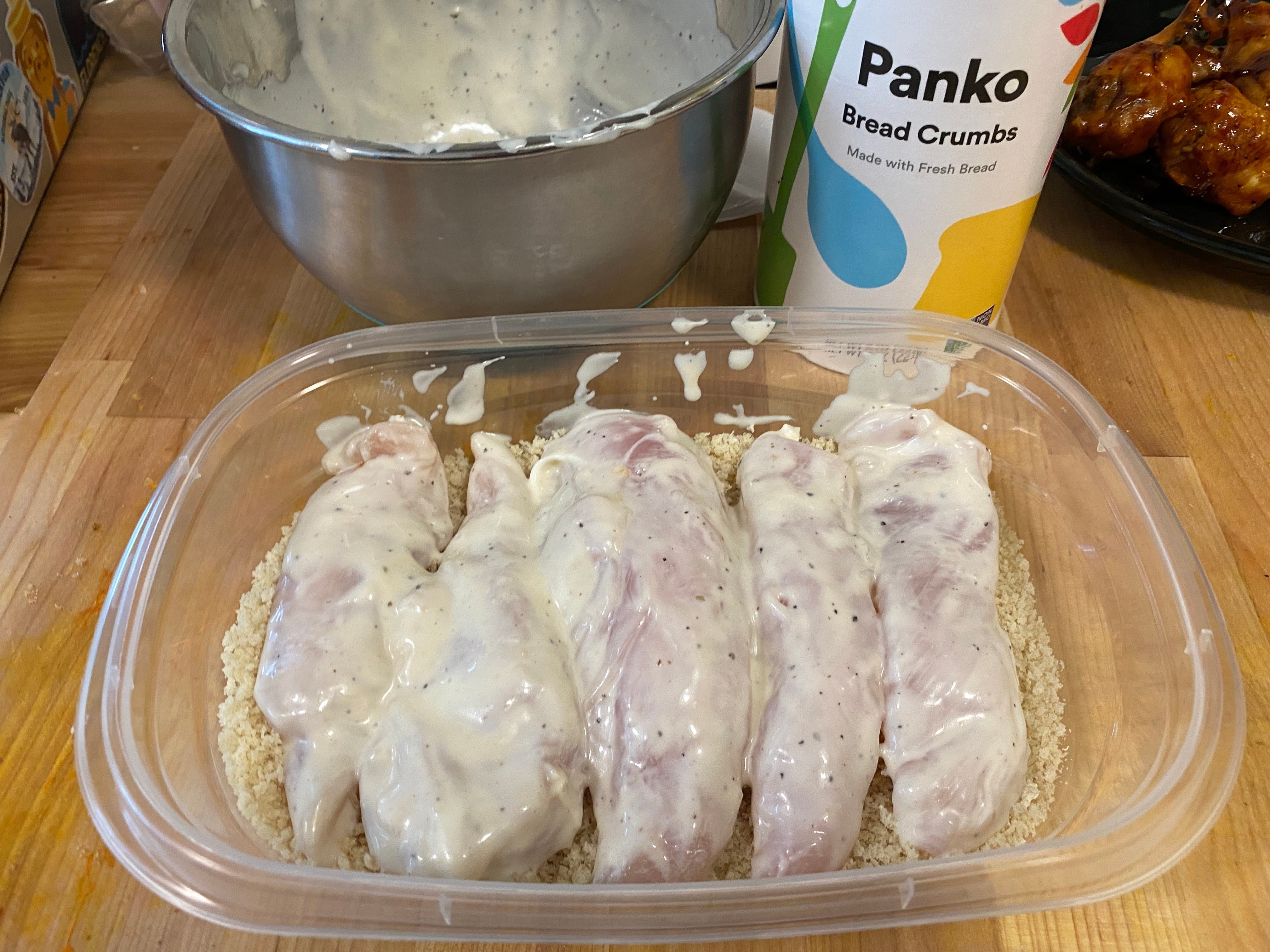 A photo of chicken tenderloins tossed in ranch marinade resting on a bed of panko bread crumbs.