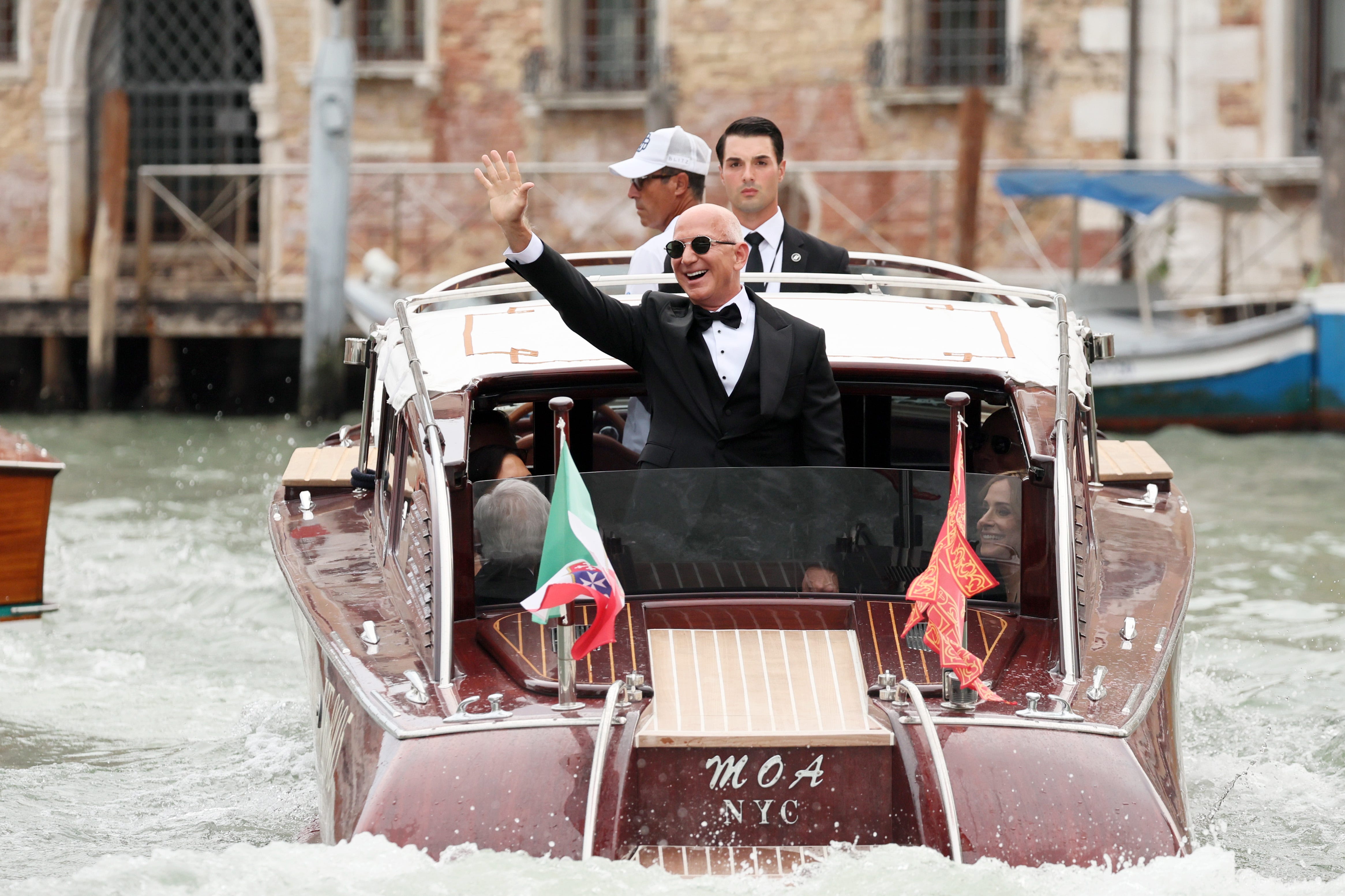 Jeff Bezos waves from a boat in Venice, wearing a tuxedo.