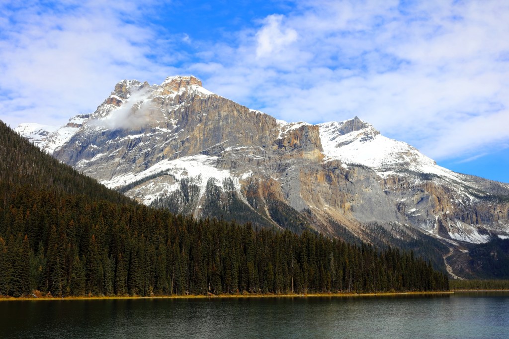 Snow-capped Rocky Mountains overlooking a lake and evergreen forest.