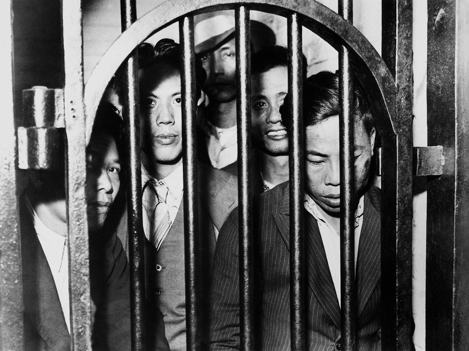 Jail bars and an archway frame a group of men.