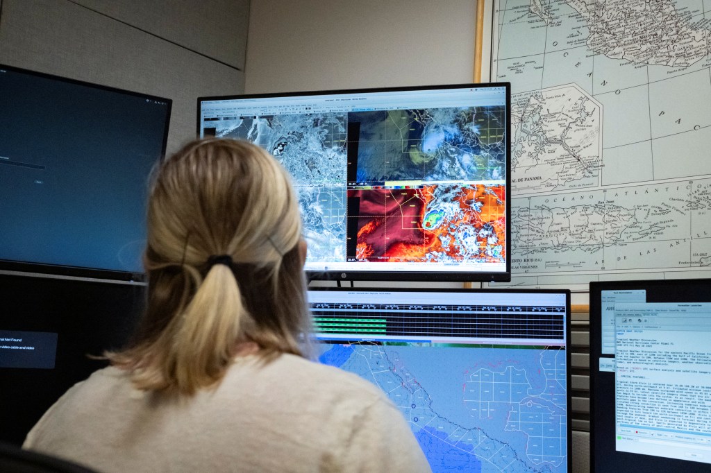 A woman views weather data on multiple computer screens.