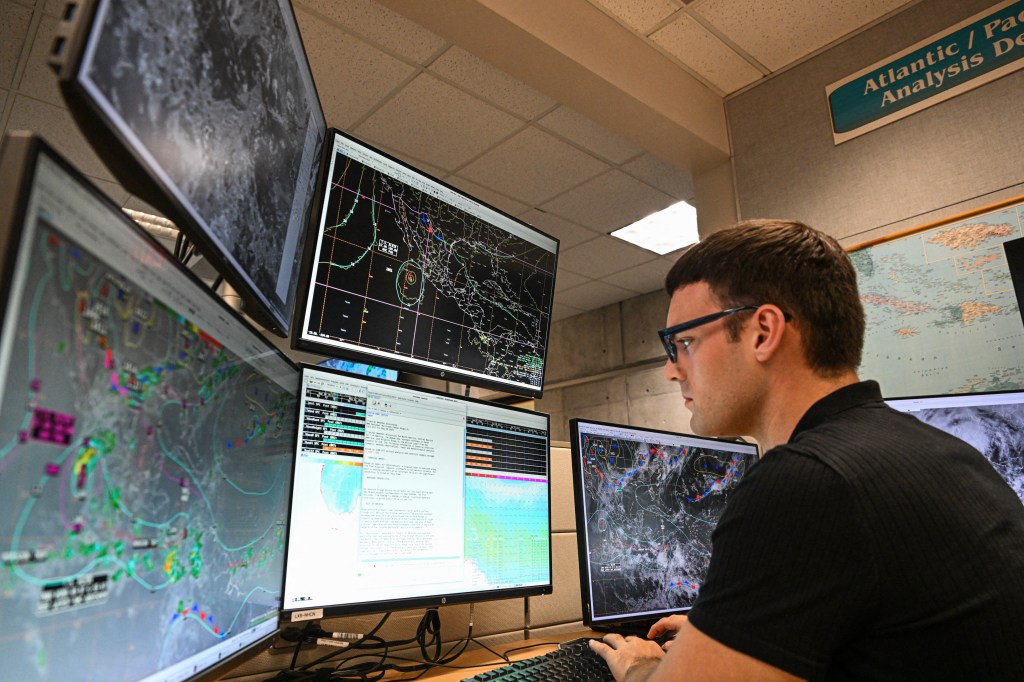 A meteorologist at the National Hurricane Center monitors weather patterns on multiple computer screens.
