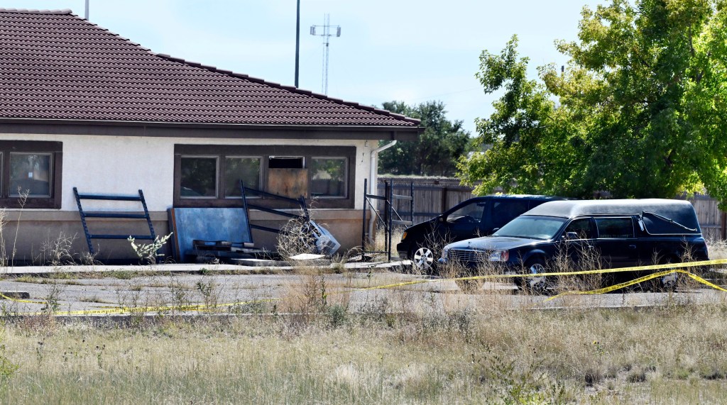 Exterior of a funeral home with a hearse and police tape.