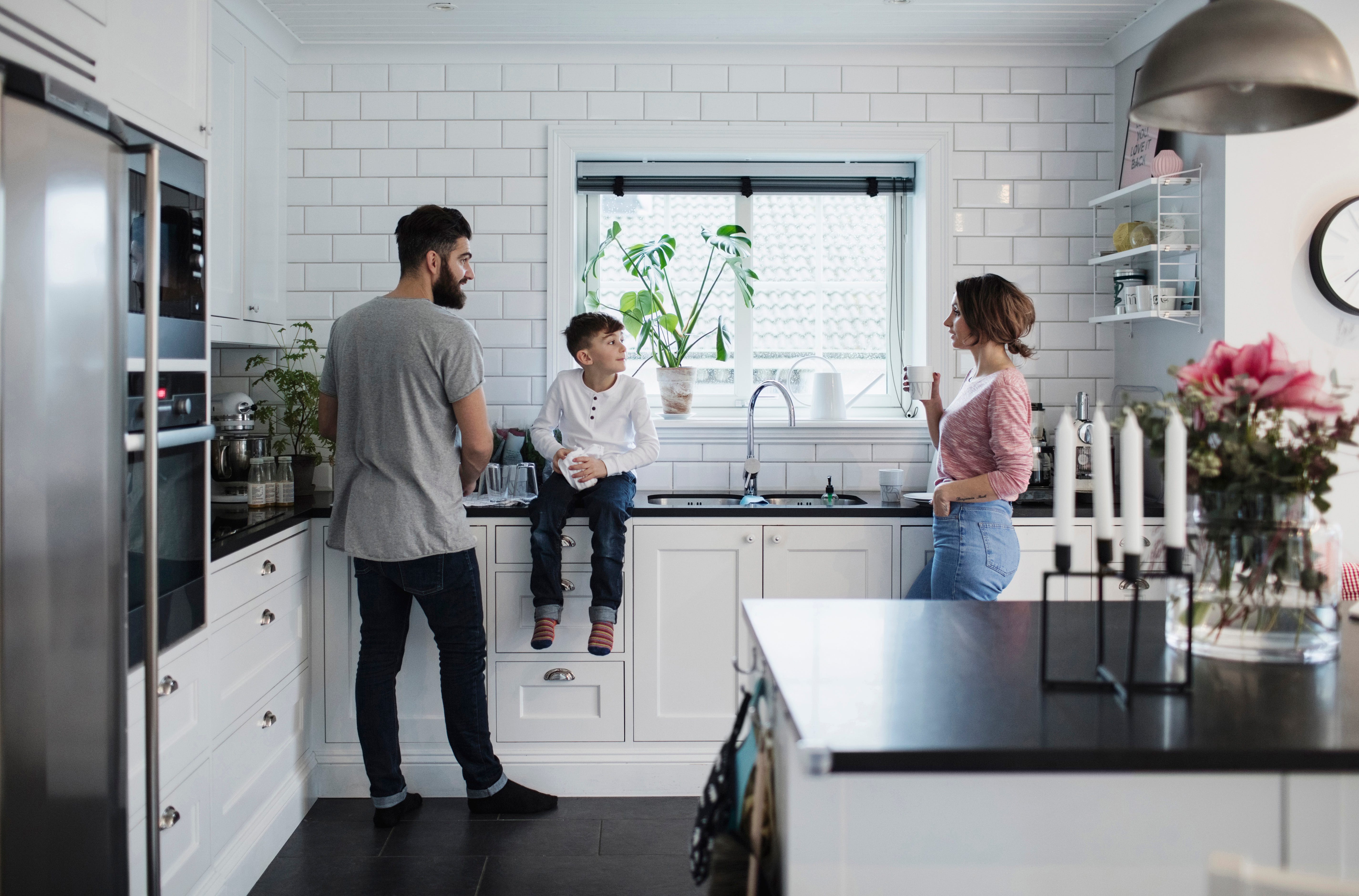 A family gathered in the kitchen. A man, small child and woman look at each other.
