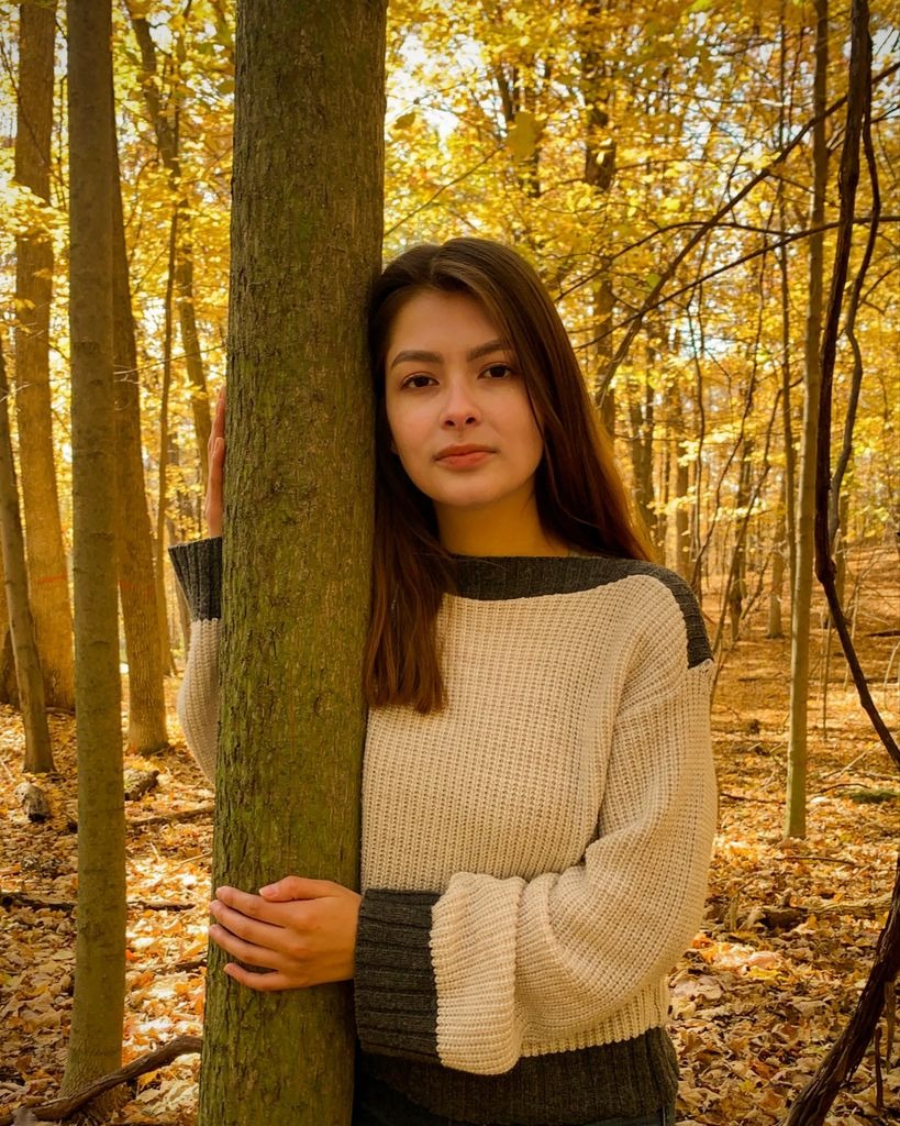 Jocelyn Jimenez leaning against a tree in an autumn forest.