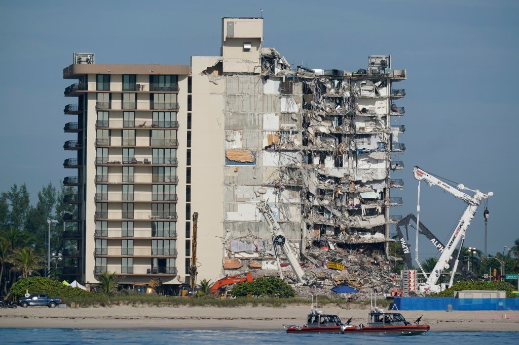 Partially collapsed building on a beach with Coast Guard boats and construction equipment.