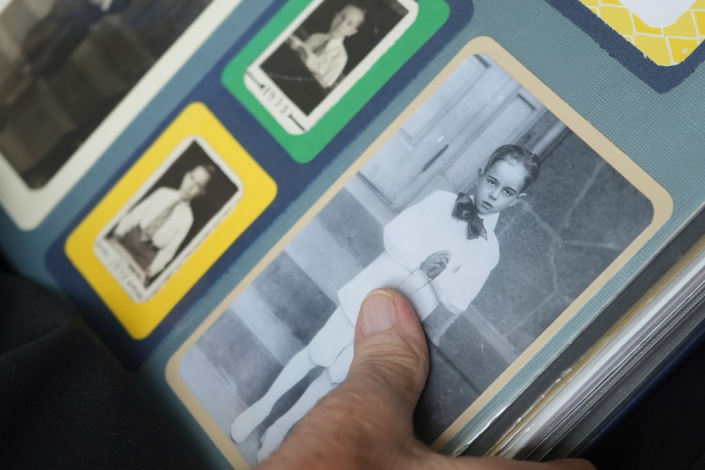 A hand points to a black and white photo of a young boy in a photo album.