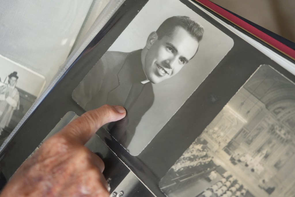 A 100-year-old priest points to a photo of himself as a young priest.