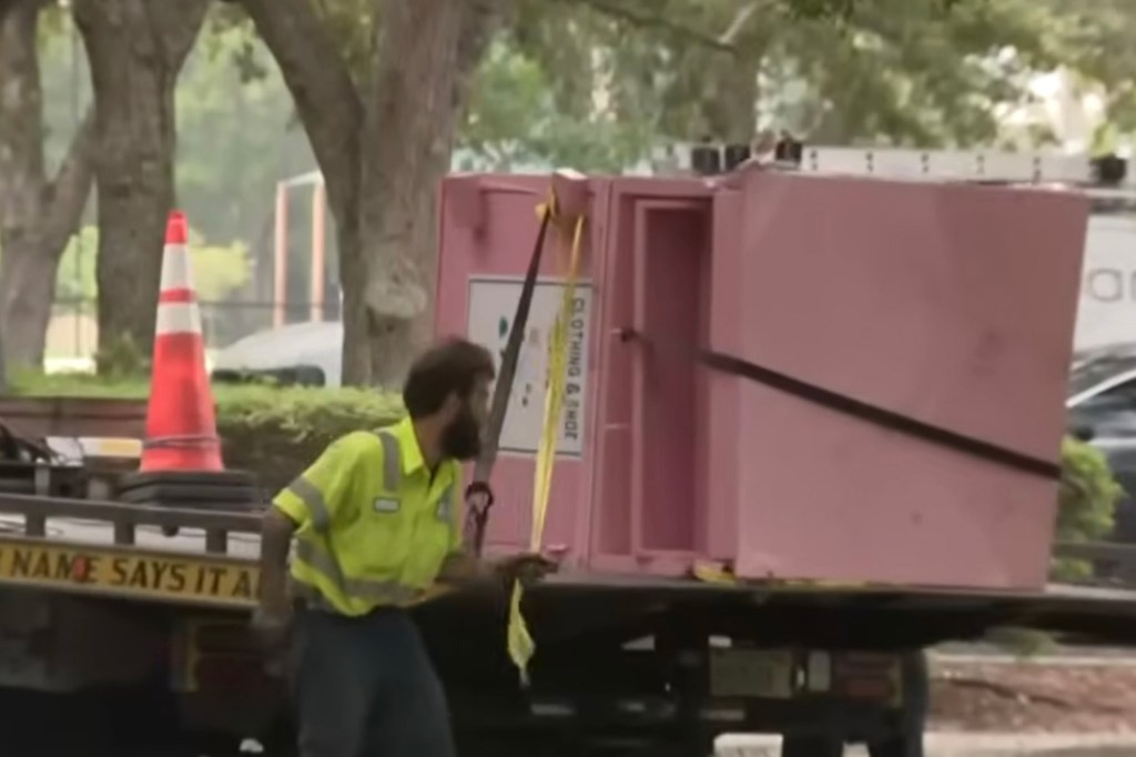 A worker loading a pink clothing donation bin onto a truck.
